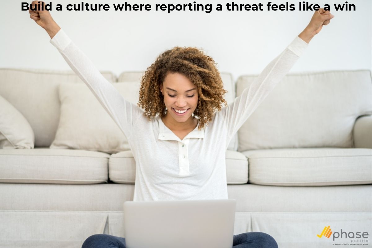 A triumphant businesswoman cheering at her laptop in a bright office, representing a positive security culture and the success of a proactive phishing strategy.